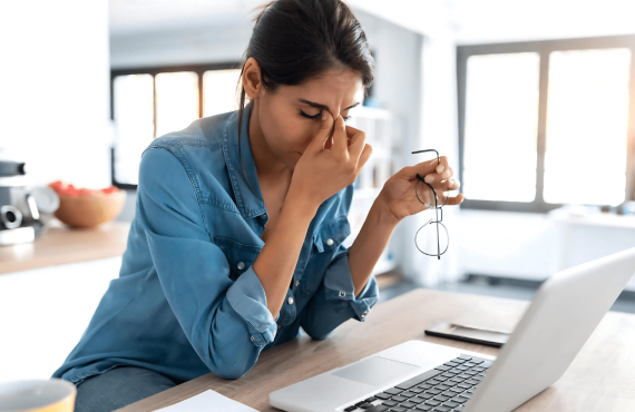 Lady in front of laptop with fingers on her eyes